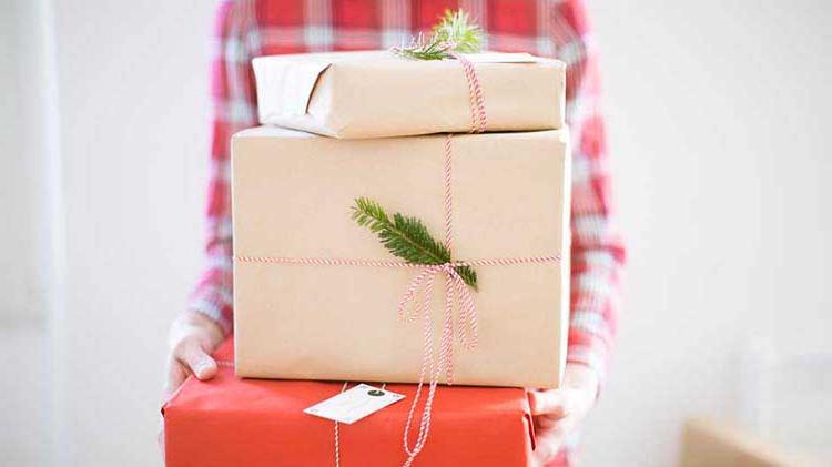 A woman holds a stack of holiday gift packages wrapped in kraft paper.