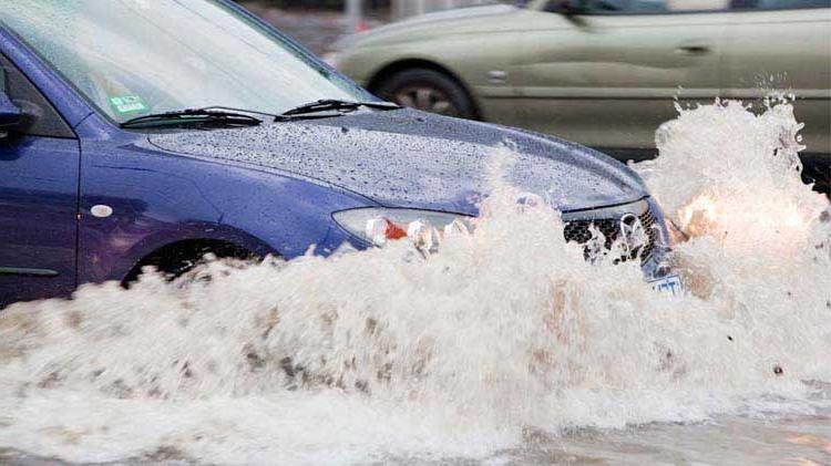 Car driving through a flooded street and possibly having flood damage as a result.