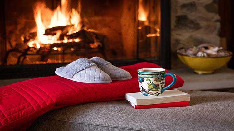 Books, hot beverage, red blanket and slippers in front of fireplace.